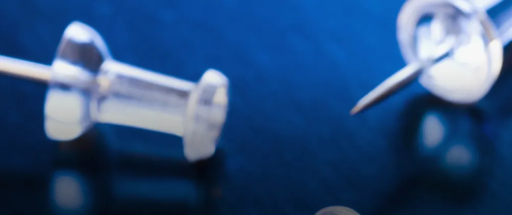 Two push pins on a wooden desk.  